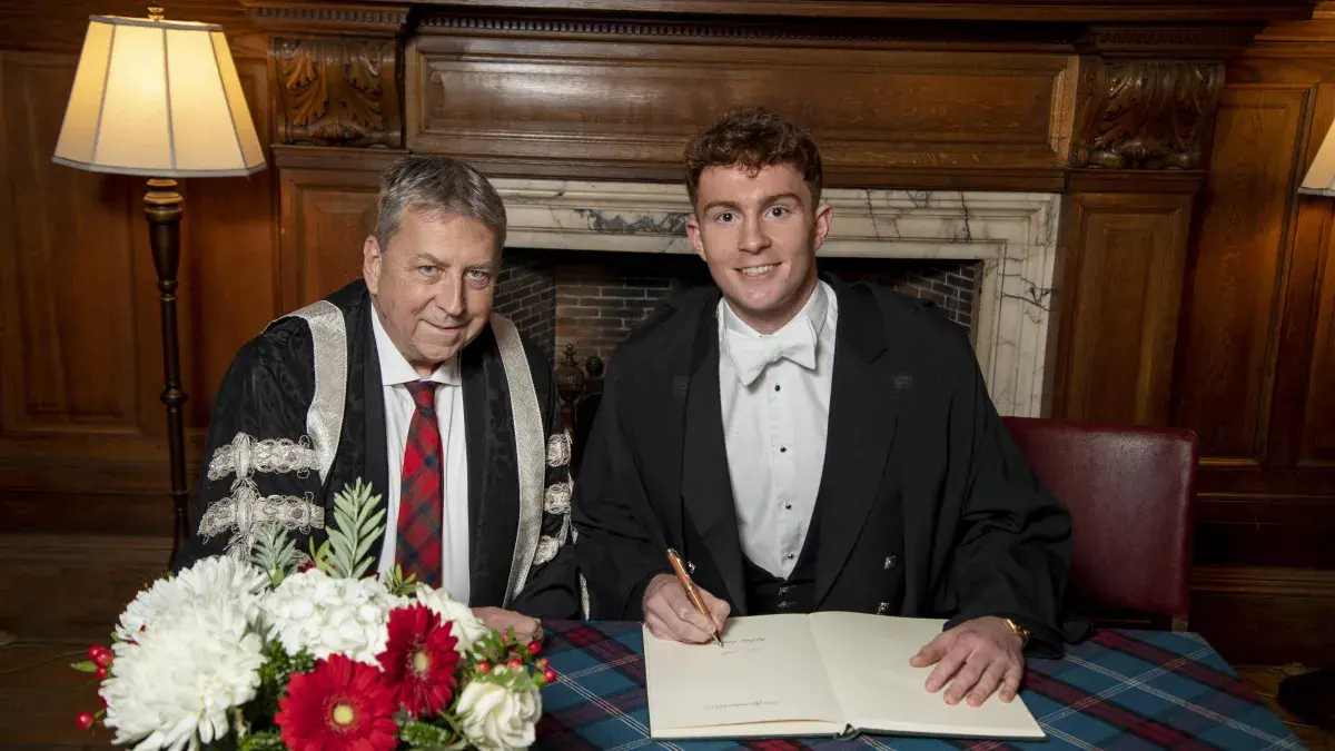 Image of Archie Goodburn sitting with Peter Mathieson signing principals medal document