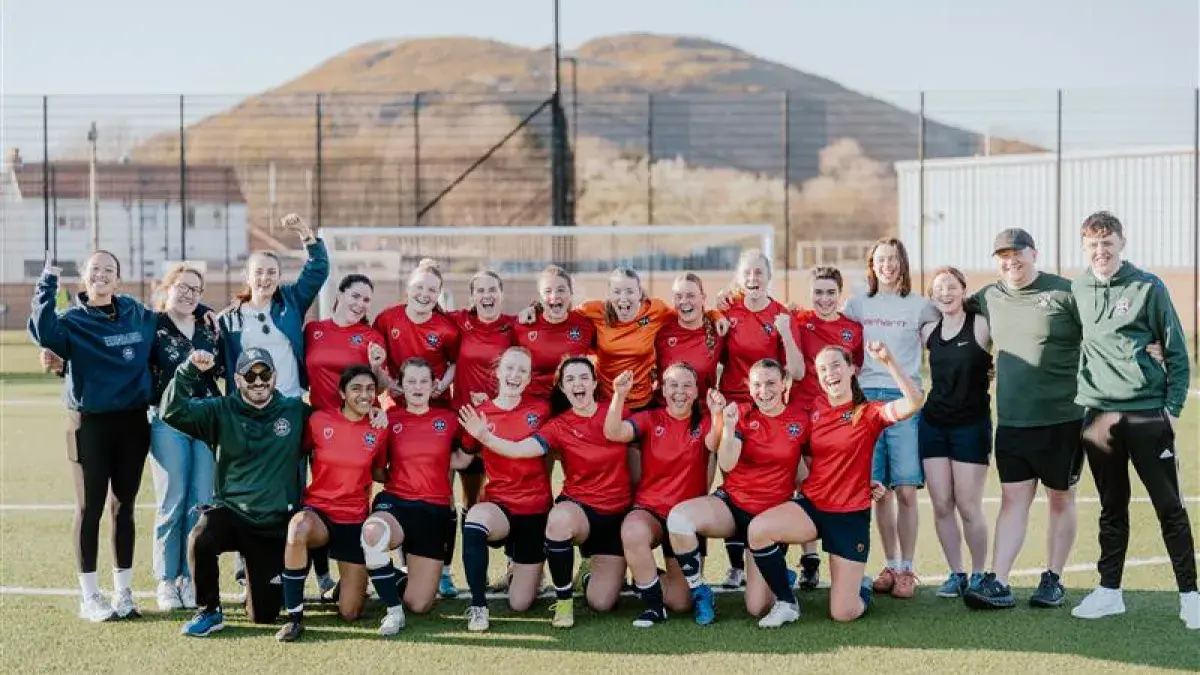 Image of women's football squad on pitch with Arthur's seat in the background
