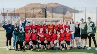 Image of women's football squad on pitch with Arthur's seat in the background