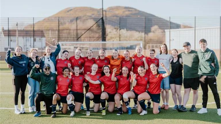 Image of women's football squad on pitch with Arthur's seat in the background