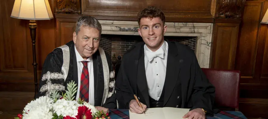 Image of Archie Goodburn sitting with Peter Mathieson signing principals medal document