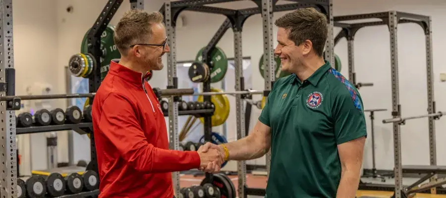 2 men shaking hands, performance gym in the background