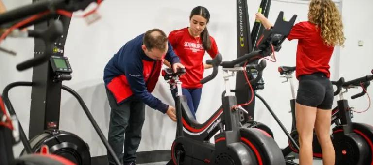 Three people gathered around gym equipment