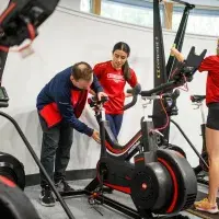 Two gym members adjusting an exercise bike whilst another works out