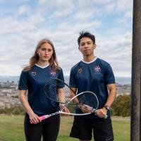 two people holding squash rackets between pillars on calton monument