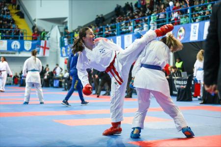 2 women competing in Karate, one kicking the other upper body