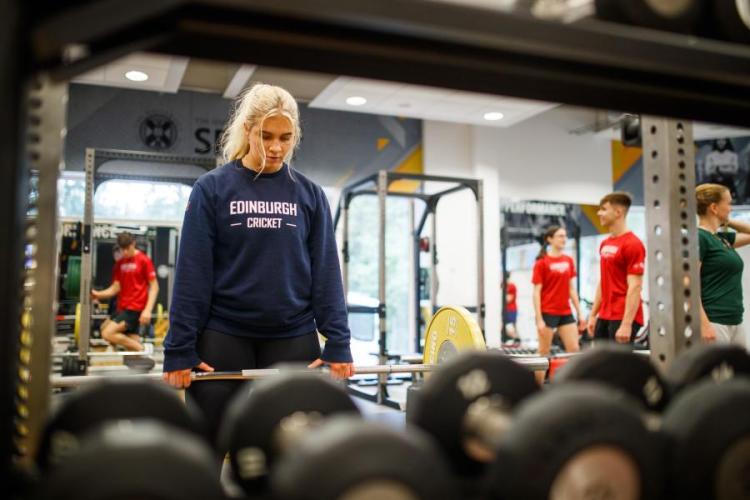 Woman in Edinburgh Cricket jumper poised to lift weight