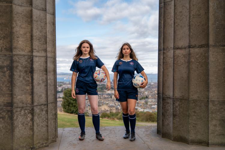 two people stood between pillars on calton monument holding footballs