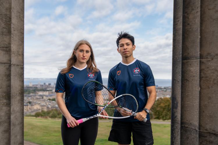 two people holding squash rackets between pillars on calton monument