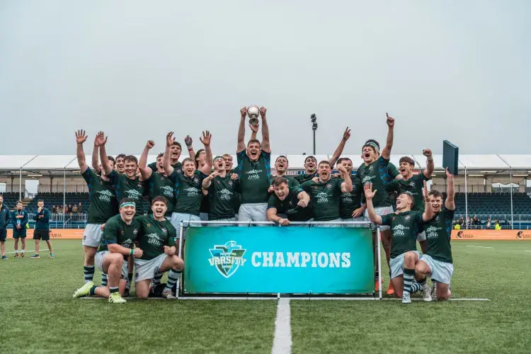men's rugby team cheering with trophy infront of champions winners board