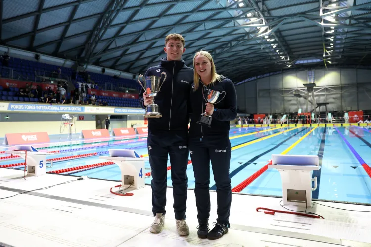2 people in front of swimming pool with trophies