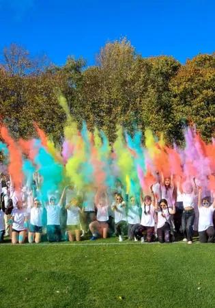 group of people in white tshirts throwing colourful paint