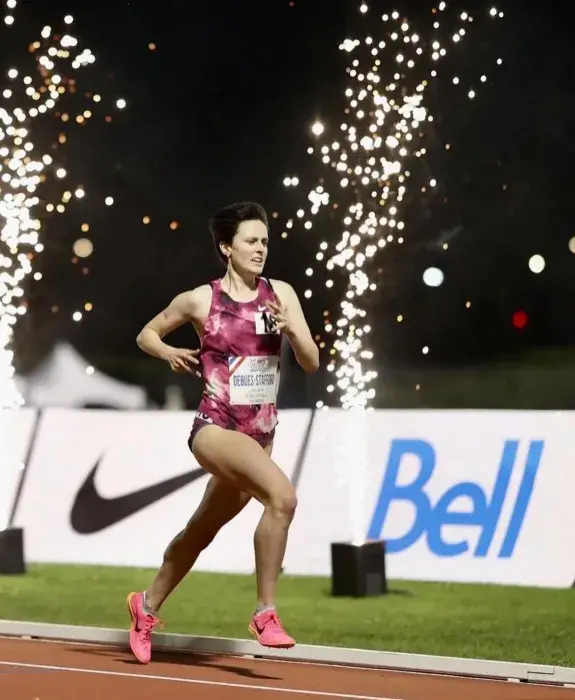 women running on athletics track with pyro sparks in the background