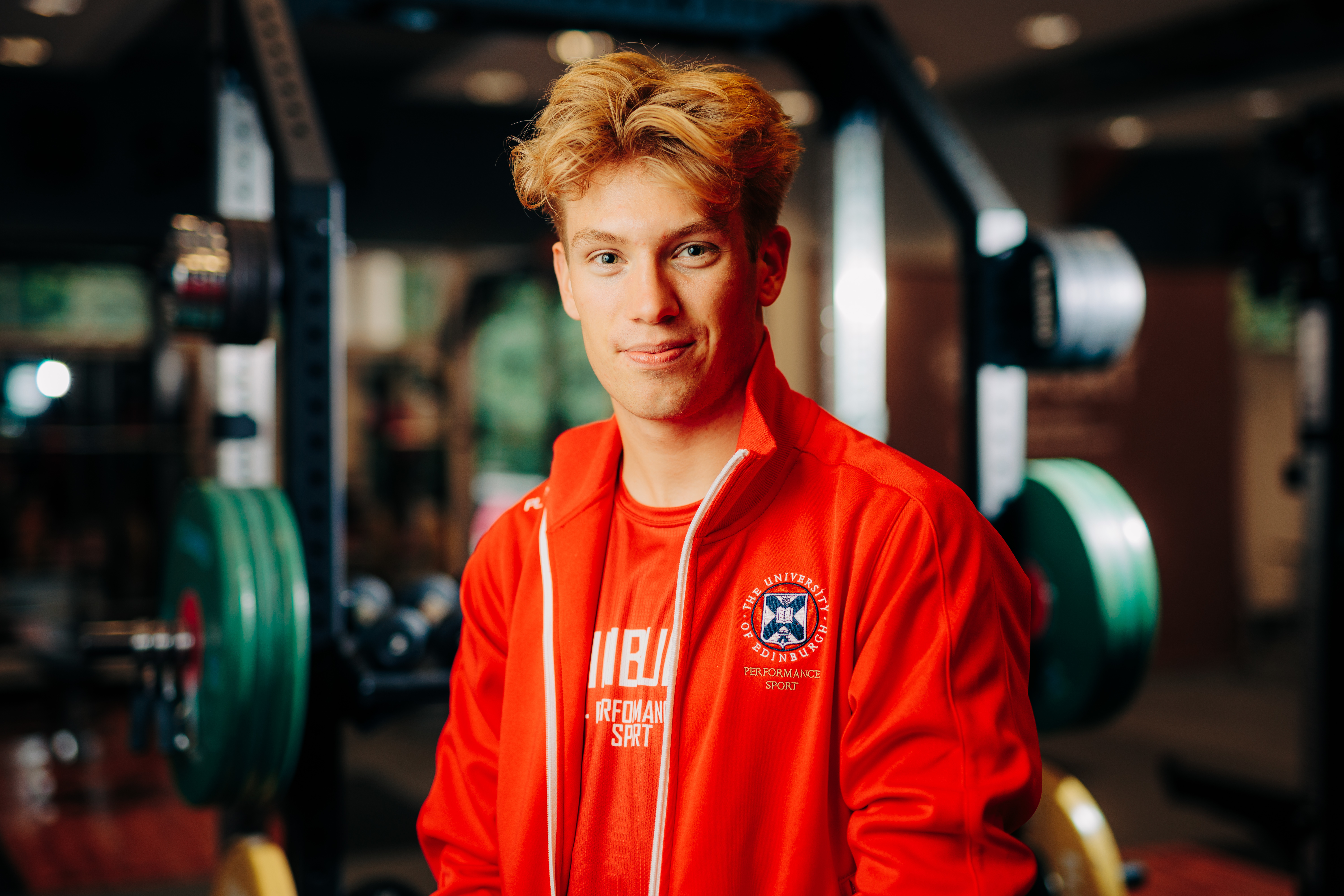 Image of sport scholar Liam Edwards smiling with gym in background