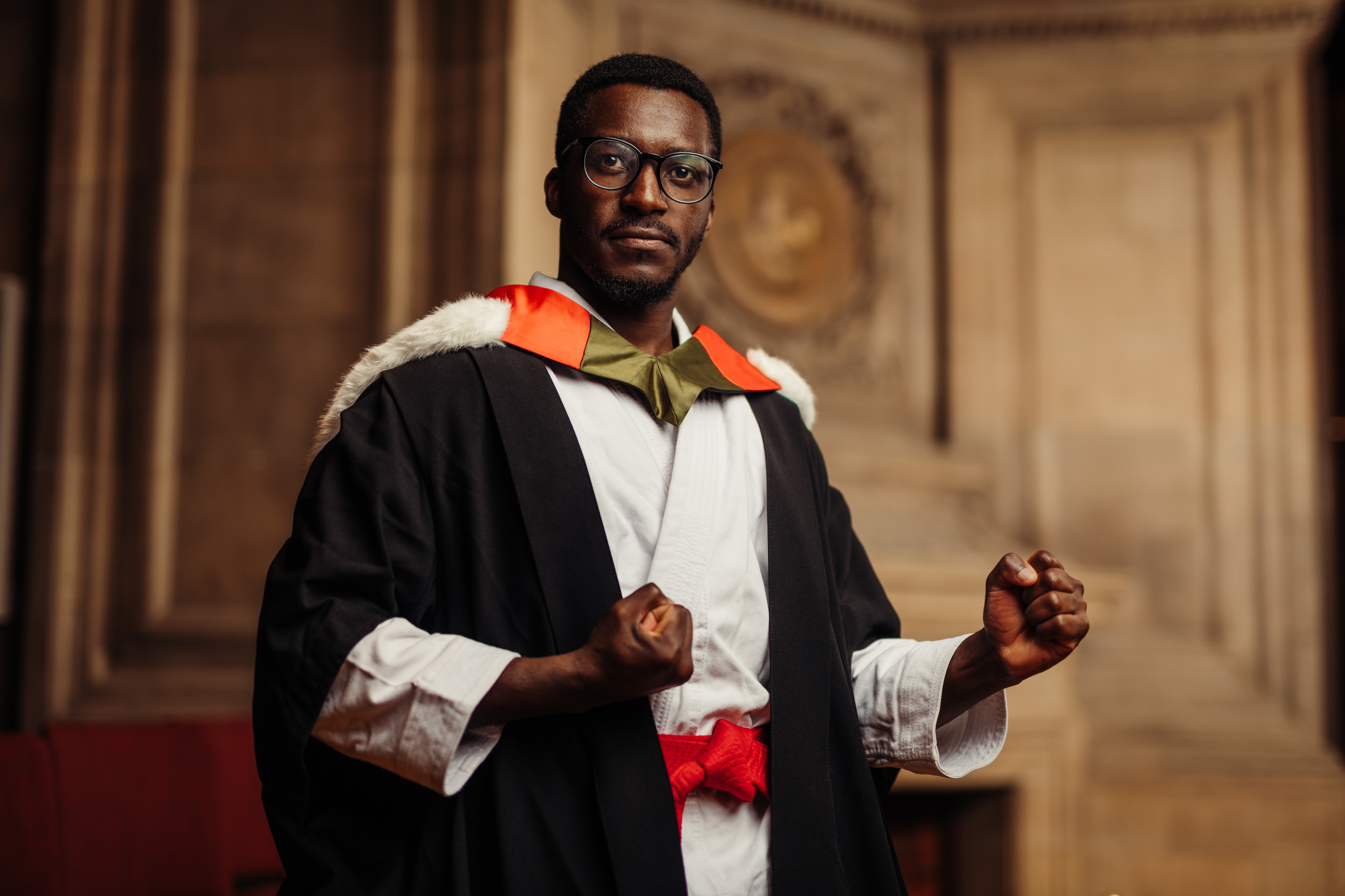 Image of man in graduation robes wearing karate kit in McEwan Hall